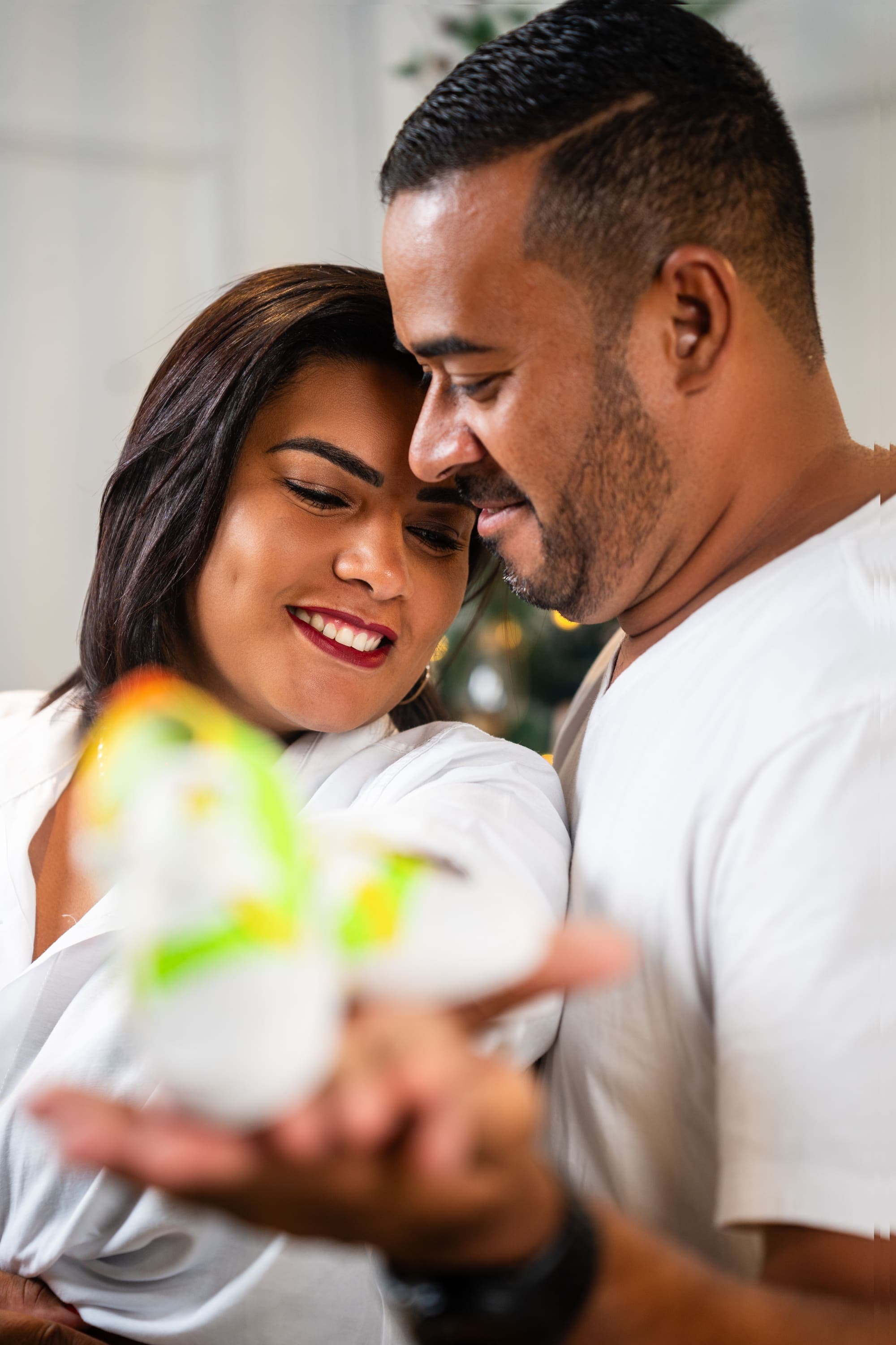 Casal grávido sorrindo, segurando um sapatinho de bebê nas mãos, decoração natalina, em Brasília